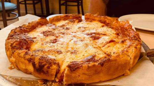 A freshly baked deep-dish pizza with melted cheese and a golden crust, served on a round tray.