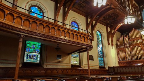 Interior of a church featuring wooden architecture, stained glass windows, and a large pipe organ.
