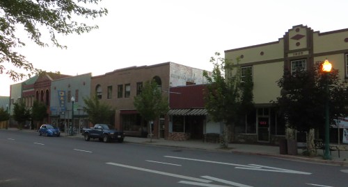 A quiet street scene featuring historic buildings, trees, and parked cars during dusk.