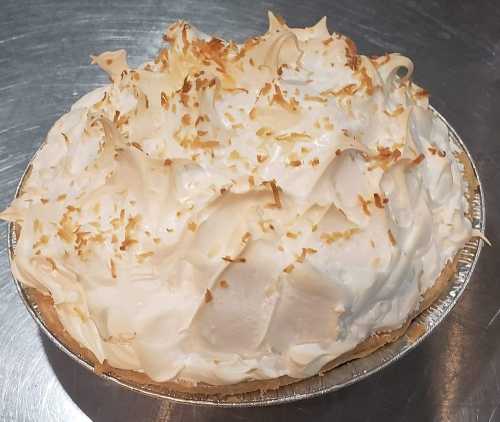 A golden-brown meringue pie topped with toasted coconut flakes in a silver pie dish.