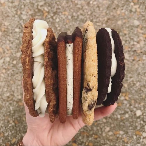 A hand holding four different ice cream sandwiches with various cookie types and fillings.