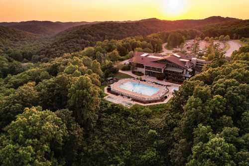 Aerial view of a resort with a pool surrounded by lush green hills at sunset.