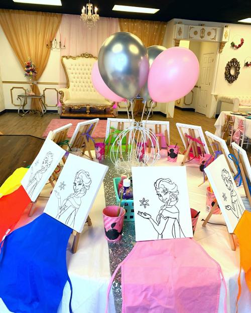 A colorful art setup with easels, balloons, and blank canvases featuring outlined characters in a decorated room.