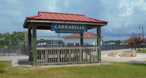 A wooden gazebo with a red roof, featuring a sign that reads "Carrabelle Get Hooked," near a waterfront.