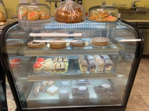 A display case filled with various baked goods, including cakes, pastries, and cookies, under glass covers.