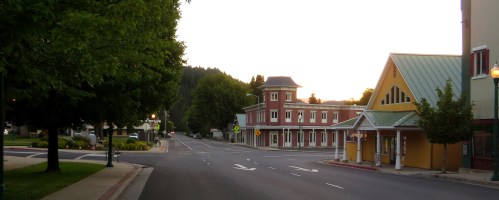 Quiet street scene at dusk, featuring charming buildings and lush trees lining the road.