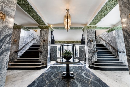 Elegant lobby with marble walls, intricate green ceiling details, and two grand staircases leading to upper levels.