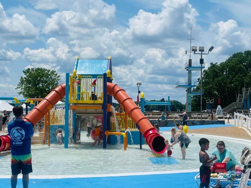A colorful water slide at a pool, with children playing and adults supervising under a sunny sky.