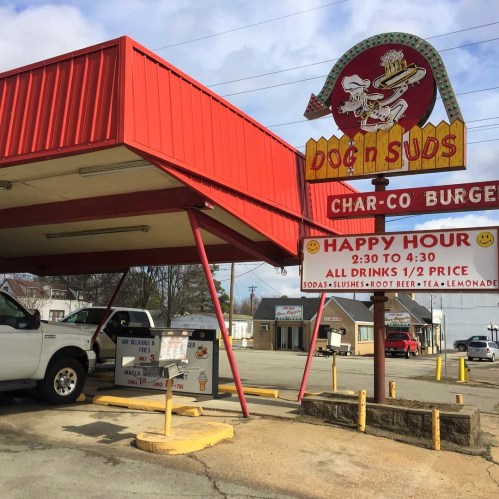 A retro drive-in restaurant sign for Dog n Suds, featuring a burger and drink specials during happy hour.