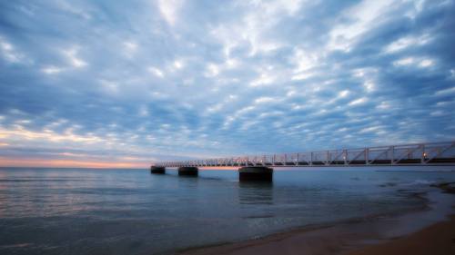 A serene beach scene featuring a long pier extending into calm waters under a cloudy sky at sunset.