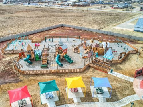 Aerial view of a colorful playground with slides, climbing structures, and shaded picnic areas in a grassy field.
