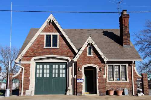 A charming brick house with a steep roof, green garage doors, and decorative trim against a clear blue sky.