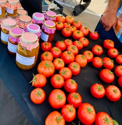 Fresh red tomatoes and jars of preserves displayed on a black table at a market.