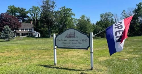 Sign for The Parker Homestead - 1665, a National Historic Site, with an "Open" flag in front of a green field.
