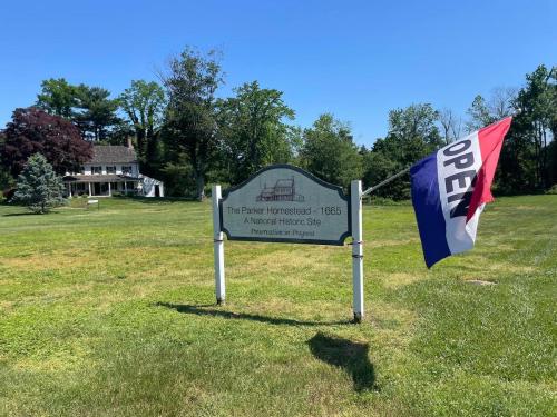 Sign for The Parker Homestead - 1665, a National Historic Site, with an open flag and a historic house in the background.