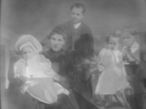 A vintage black-and-white photo of a woman holding a baby, with three children standing nearby.