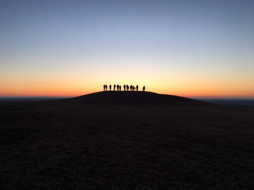 Silhouetted figures stand on a hilltop against a vibrant sunset sky.