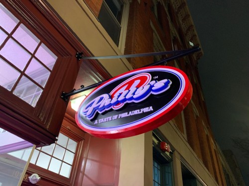 Neon sign for "Philly's: A Taste of Philadelphia" hanging outside a building at night.