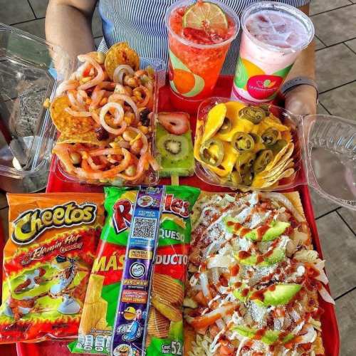 A colorful food tray featuring snacks, nachos, fruit, and drinks, held by a person.