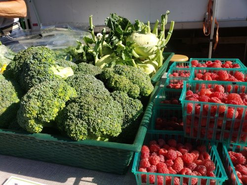 A market display featuring fresh broccoli and baskets of raspberries.