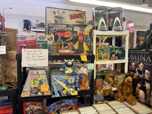 A display of vintage toys and collectibles, including Transformers, action figures, and comic books, in a store setting.