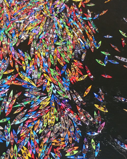Aerial view of a vibrant gathering of colorful kayaks and canoes on a dark water surface.