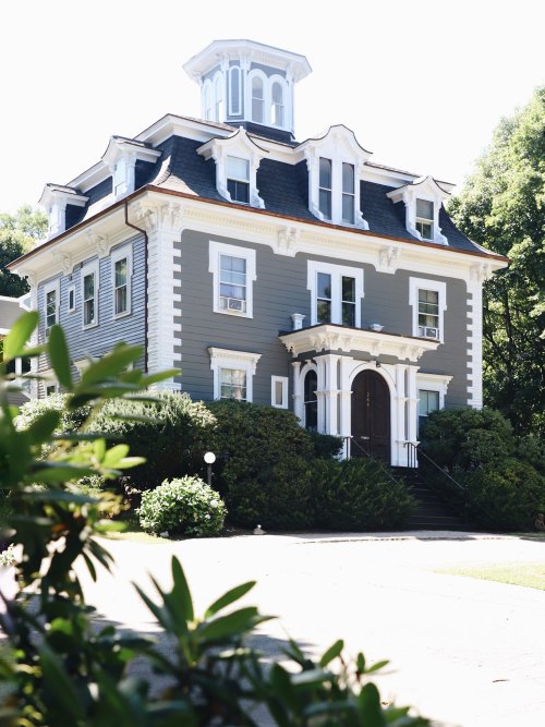 A large, elegant gray house with a tower and intricate architectural details, surrounded by greenery.