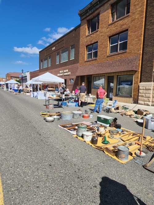 A bustling street market with vendors selling various items, including antiques and crafts, under a clear blue sky.