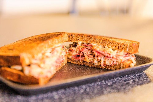 A close-up of a sliced sandwich with layers of meat and cheese on dark bread, served on a black plate.