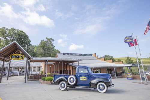 A vintage blue truck parked in front of the A.J. Bush Co. building, with flags and greenery in the background.