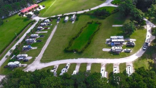 Aerial view of a campground with RVs parked along winding paths and a green lawn in the center.