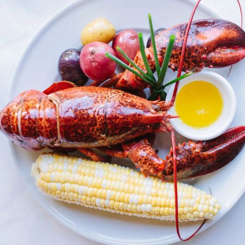 A plate featuring two lobsters, corn on the cob, potatoes, and a small bowl of melted butter.