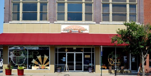Exterior of Prairie Harvest Market with large windows and a red awning, featuring colorful signage and plants outside.