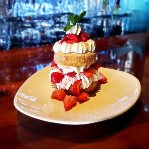 A stacked dessert featuring donuts, whipped cream, and fresh strawberries on a plate.