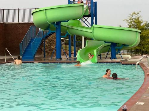 A swimming pool with a green water slide; people are swimming and enjoying the water.