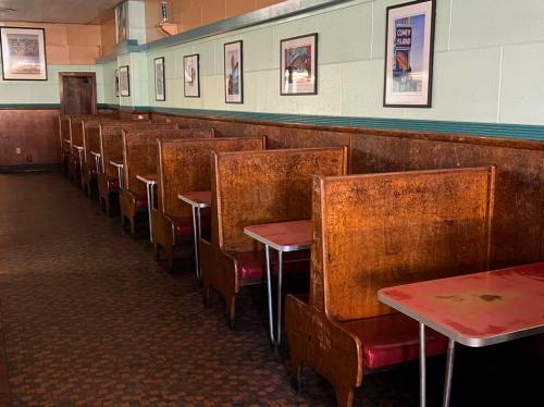 Empty diner interior with wooden booths and tables, framed pictures on the walls, and a patterned floor.