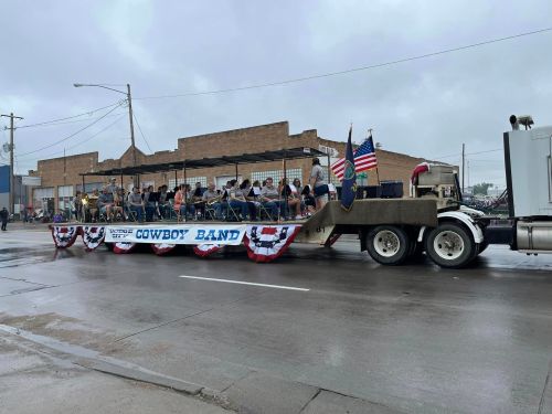 A parade float featuring a cowboy band, decorated with red, white, and blue, on a rainy street.