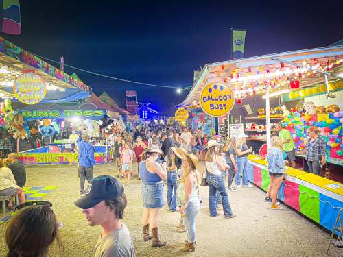 A lively night scene at a fair, with colorful game booths and crowds enjoying various attractions and activities.