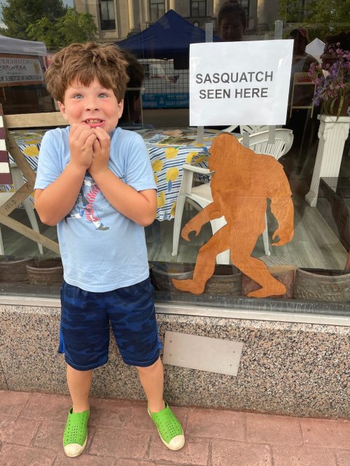 A surprised boy stands by a window with a Sasquatch cutout and a sign that says "Sasquatch Seen Here."