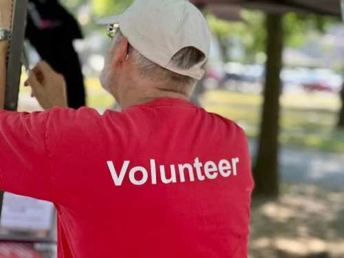 A person wearing a red shirt with "Volunteer" printed on the back, working at an outdoor event.