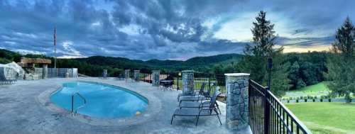 A serene pool area with lounge chairs, surrounded by lush hills and a dramatic sky at dusk.