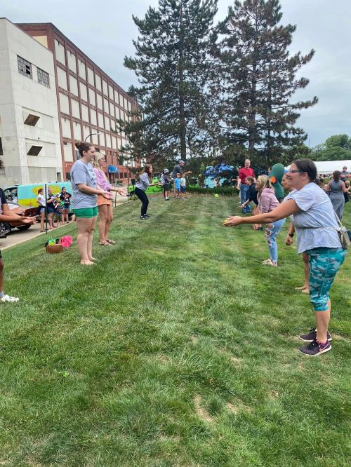 A group of people participate in a fun outdoor game on a grassy field, with spectators watching nearby.