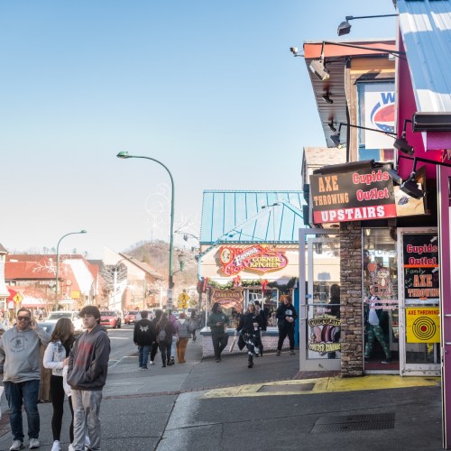 A busy street scene with people walking, shops, and a blue bridge in the background on a sunny day.