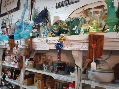 A display of colorful glassware and vintage items on shelves in a quaint shop, with price tags and decorative accents.