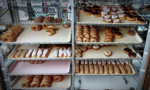 A display of assorted donuts on metal racks, featuring glazed, chocolate, and cream-filled varieties.