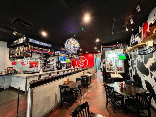 Interior of a casual restaurant with a bar, tables, and sports-themed decor, featuring a vibrant atmosphere.