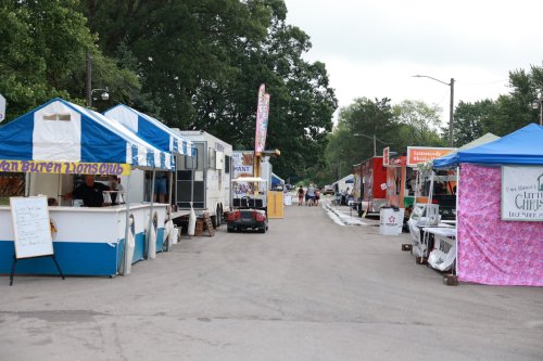 A street lined with food vendor tents, featuring colorful canopies and a cloudy sky above.