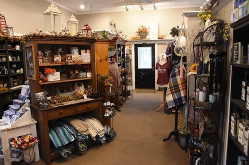 A cozy shop interior filled with shelves of home decor, gifts, and seasonal items, leading to a black door.