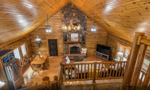 Cozy log cabin interior with wooden beams, stone fireplace, dining area, and modern amenities. Warm and inviting atmosphere.