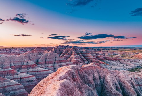 Vibrant sunset over layered rock formations in a vast, rugged landscape with colorful skies.